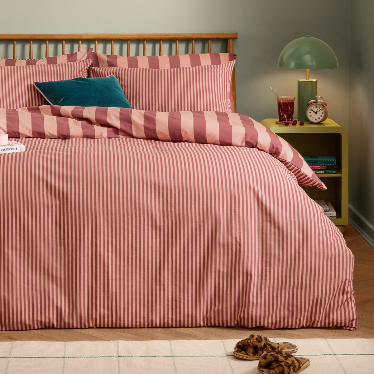 Reversible striped duvet cover set in Raspberry Smoothie pink tones, dressed on a bed with matching pillowcases and a teal accent cushion in a bedroom setting.
