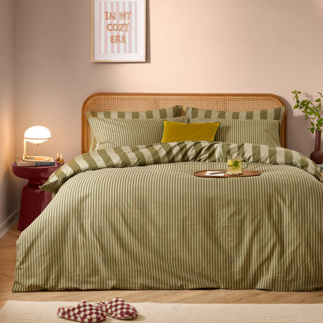 Green tea striped reversible cotton duvet cover set styled on a bed with matching pillowcases and a rattan headboard in a pink-toned bedroom.