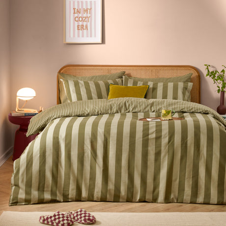 Green tea striped reversible cotton duvet cover set on a bed with rattan headboard, styled with a mustard cushion in a cosy pink bedroom setting.