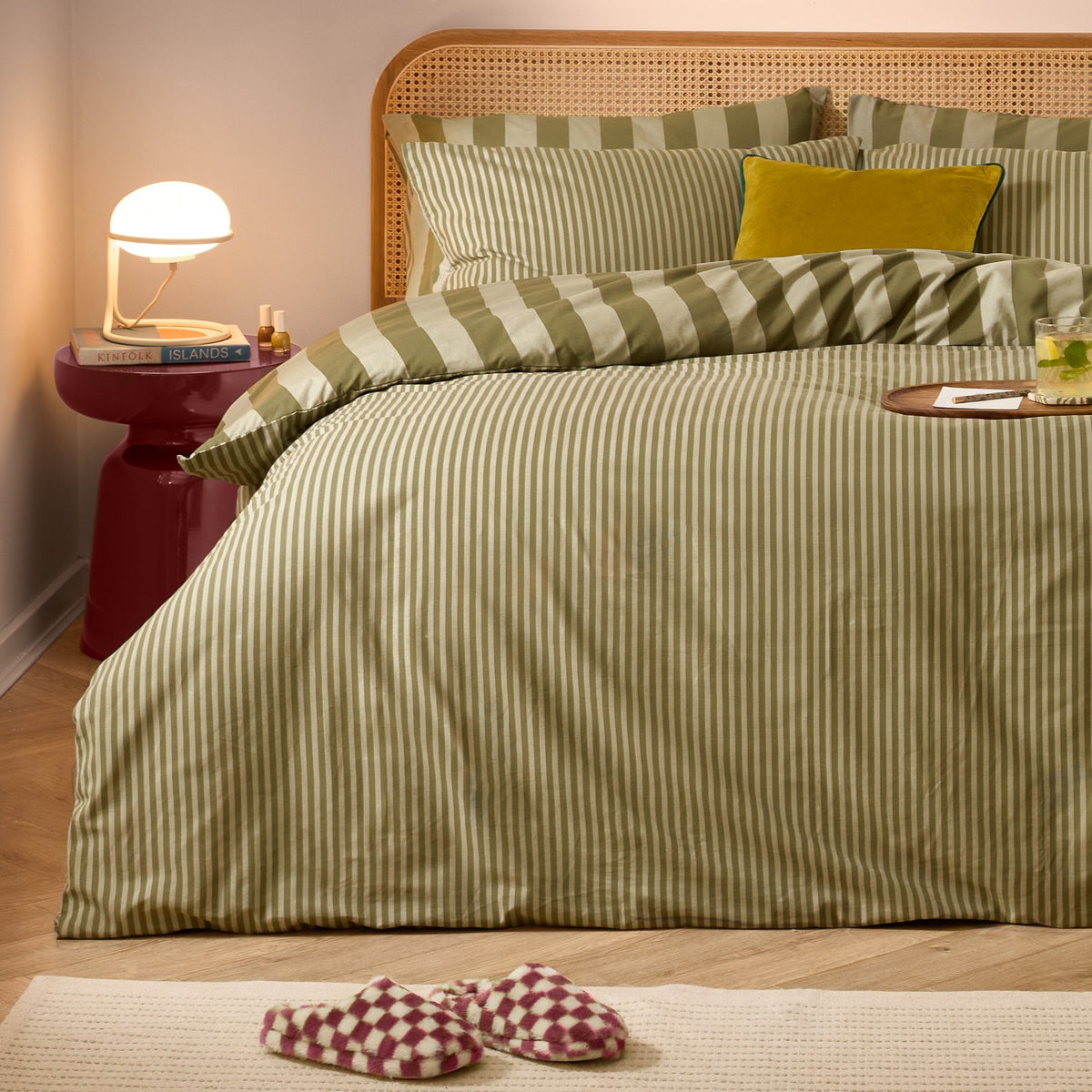 The Ultimate Stripe Cotton Reversible Duvet Cover Set in Green Tea dresses a rattan headboard bed with narrow-striped pillowcases and a mustard cushion in a cosy bedroom setting.