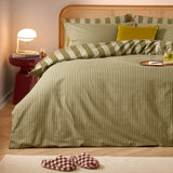 The Ultimate Stripe Cotton Reversible Duvet Cover Set in Green Tea dresses a rattan headboard bed with narrow-striped pillowcases and a mustard cushion in a cosy bedroom setting.