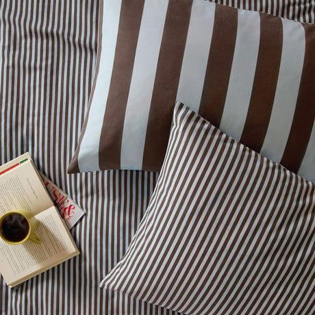 Ultimate Stripe cotton blend pillowcase pair in Blueberry Muffin, shown on a bed with matching striped duvet, brown-and-blue stripes, styled with a book and coffee mug.