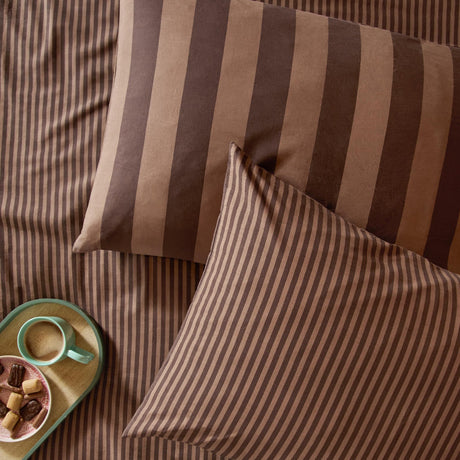 The Ultimate Stripe Cotton Blend Pillowcase Pair in Chocolate Truffle, shown with wide and narrow brown stripe designs on a bed, styled with a tray, mug, and biscuits.