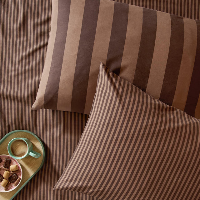 The Ultimate Stripe Cotton Blend Pillowcase Pair in Chocolate Truffle, shown with wide and narrow brown stripe designs on a bed, styled with a tray, mug, and biscuits.