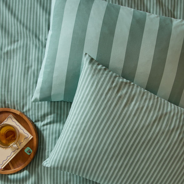 The Ultimate Stripe Cotton Blend Pillowcase Pair in peppermint green, shown reversible with narrow and bold stripe sides on bedding.