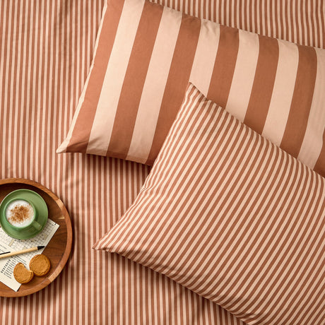 The Ultimate Stripe Cotton Blend Pillowcase Pair in Pumpkin Spice, shown on a bed with matching striped bedding, styled with a tray, coffee cup, and biscuits.