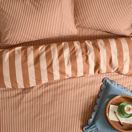 Bedroom styling shot of The Ultimate Stripe Cotton Blend Pillowcase Pair in Pumpkin Spice, showing reversible narrow and bold orange-and-cream stripes with matching striped duvet bedding.