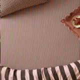 Ultimate Stripe Cotton Blend Fitted Sheet in Berry Brownie, fitted on a bed showing pink and chocolate brown striped fabric, with a scalloped tray of brownies alongside.