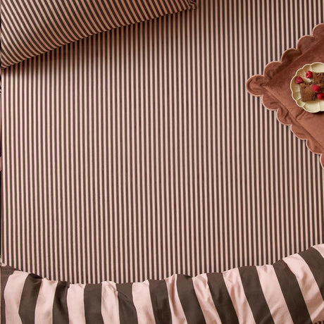 Ultimate Stripe Cotton Blend Fitted Sheet in Berry Brownie, fitted on a bed showing pink and chocolate brown striped fabric, with a scalloped tray of brownies alongside.