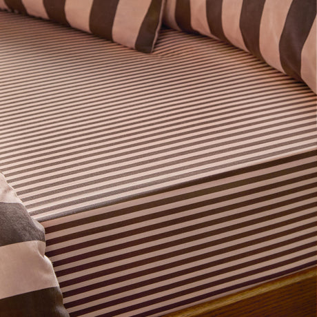 Fitted sheet in a fine pink and brown tonal stripe cotton blend, shown on a mattress with matching striped pillows in the background.