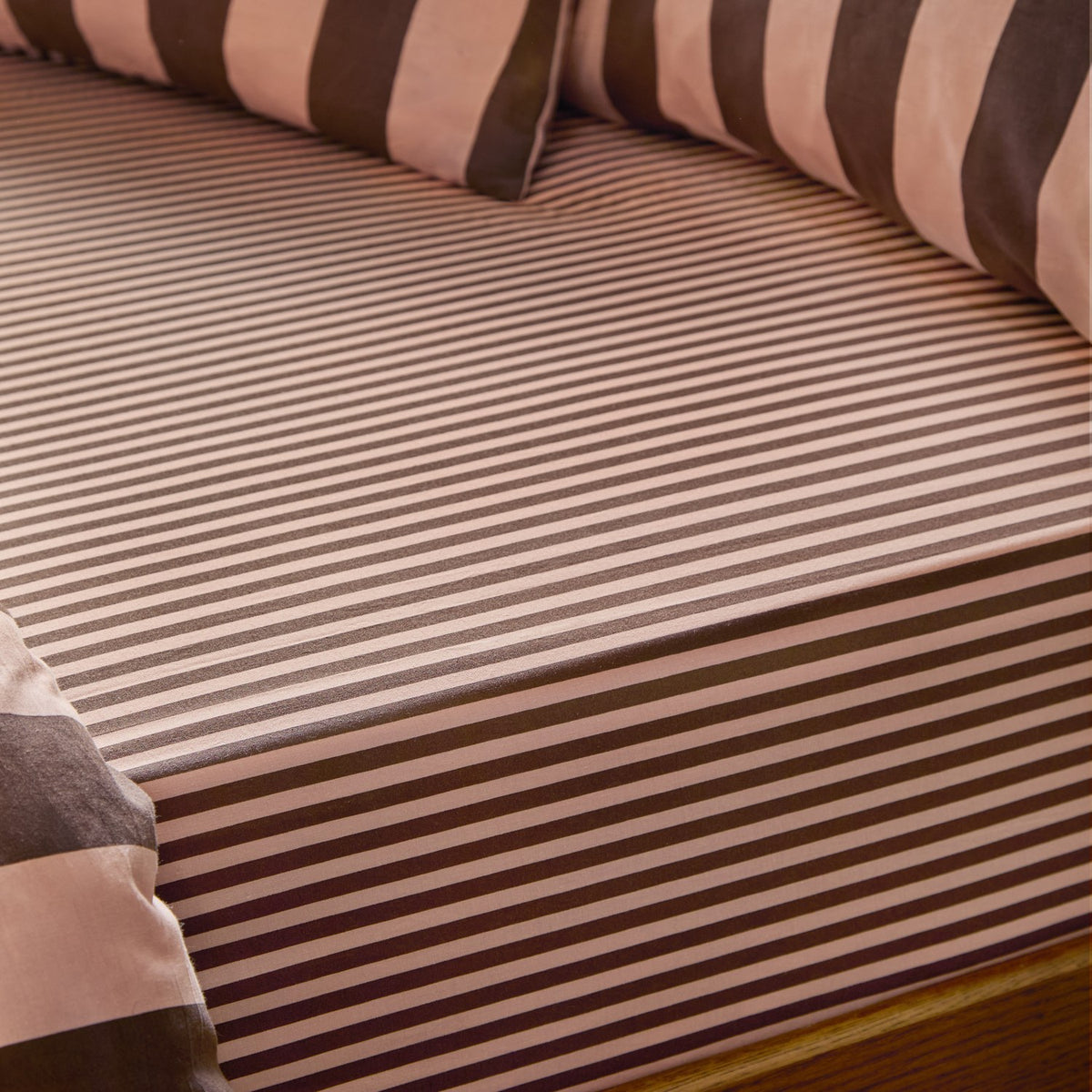 Fitted sheet in Berry Brownie tonal stripe, pink and chocolate brown cotton-polyester blend, shown on a bed with matching striped pillowcases.