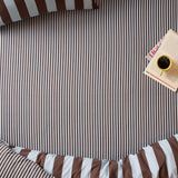 The Ultimate Stripe Cotton Blend Fitted Sheet in Blueberry Muffin, brown and white pinstripe fitted sheet on a bed with matching pillowcase, styled with a book and coffee cup.