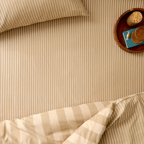 The Ultimate Stripe Cotton Blend Fitted Sheet in Caramel Latte, shown on a bed with a matching pillowcase in a tonal beige stripe, styled beside a wooden tray with drinks and waffles.