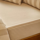 Close-up of The Ultimate Stripe Cotton Blend Fitted Sheet in Caramel Latte, showing tonal beige stripes and elasticated corner fitted on a mattress with matching pillowcases.