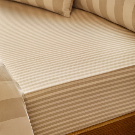 Close-up of The Ultimate Stripe Cotton Blend Fitted Sheet in Caramel Latte, showing tonal beige stripes and elasticated corner fitted on a mattress with matching pillowcases.