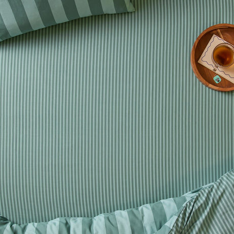 The Ultimate Stripe Cotton Blend Fitted Sheet in Peppermint on a bed with matching pillowcase, styled with a wooden tray, drink, and notepad.