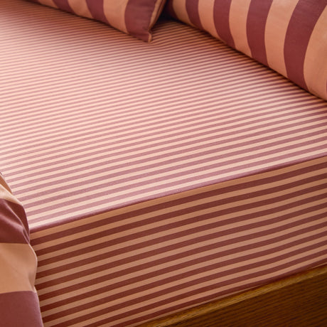The Ultimate Stripe Cotton Blend Fitted Sheet in Raspberry Smoothie, fitted on a bed with matching striped pillows in a tonal pink and burgundy narrow stripe pattern.