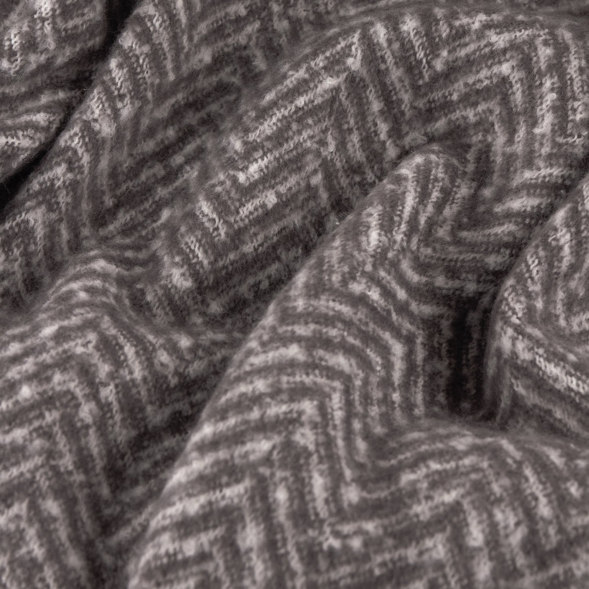 Close-up of the Tweedie Herringbone Polyester Throw in charcoal, showing the folded fabric with a two-tone grey chevron weave pattern.