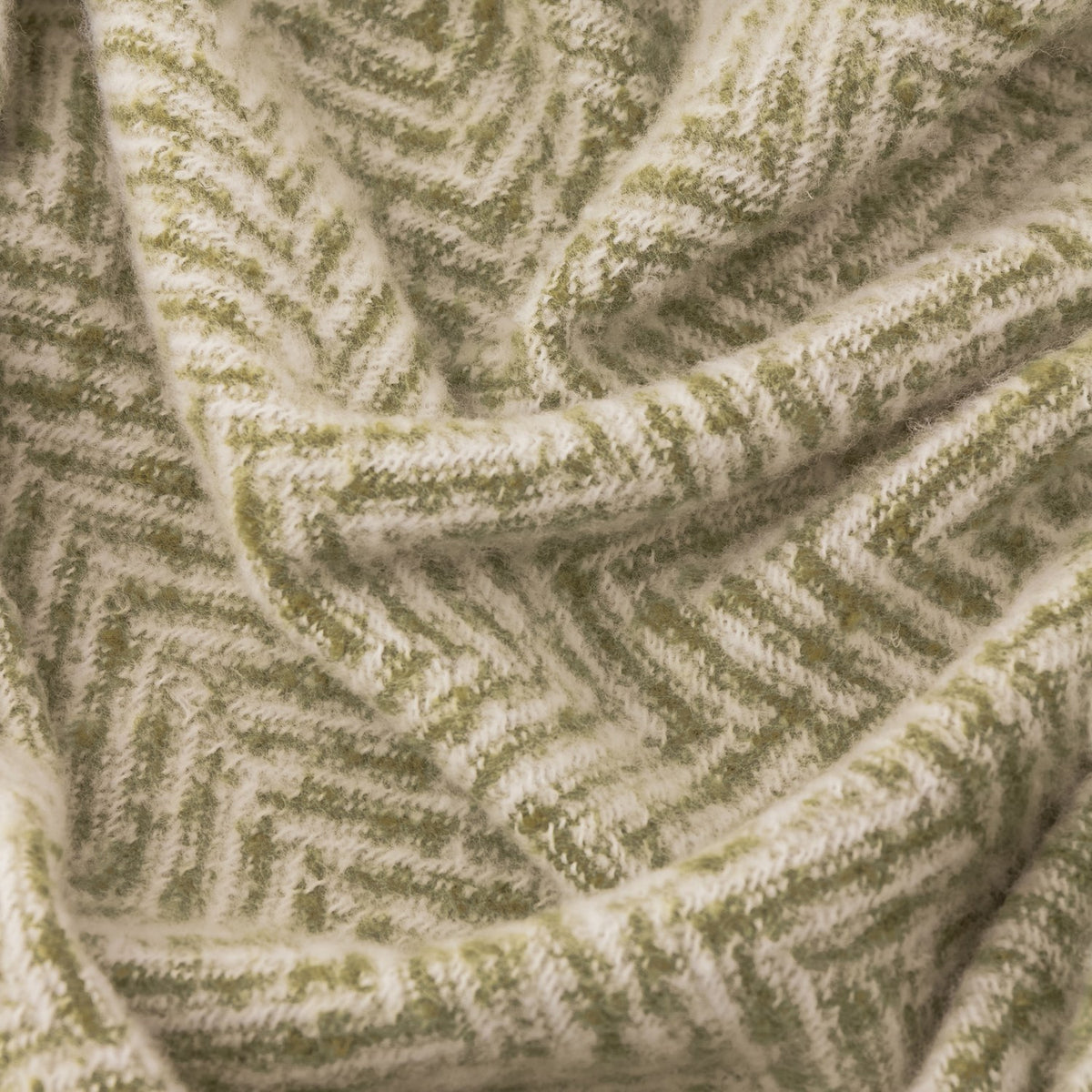 Close-up of the Tweedie Herringbone Polyester Throw in green, showing the woven zigzag pattern in green and cream fabric.