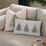Square natural linen-look cushion with an embroidered green fir tree, gold stars and red baubles, edged in red piping, shown on a sofa beside a rectangular tree-print cushion.