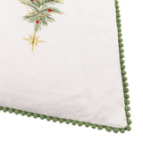 Corner detail of the Twinkling Tree Woodland Velvet Cushion in cream, showing embroidered pine, berries, a gold star, and green pompom trim edging.