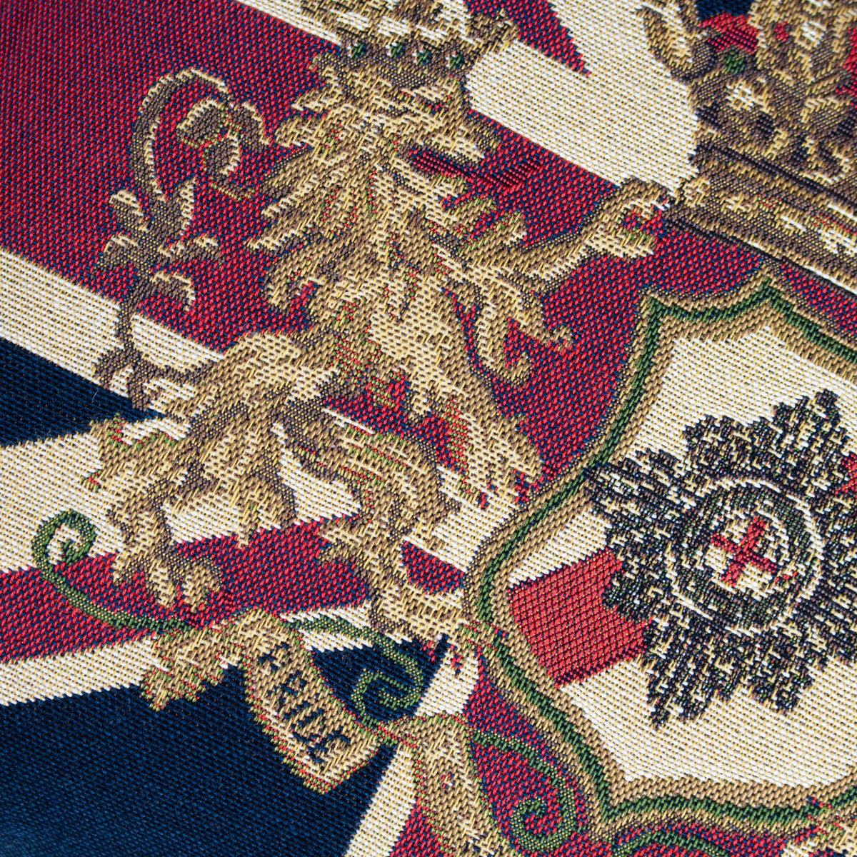 Close-up of the Union Jack Jacquard Cotton Cushion showing woven cotton jacquard detail with a gold lion crest, crown and shield motif on navy, red and cream ground.
