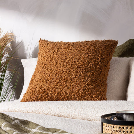 Ulsmere Wool Cotton Cushion in Ginger, a square cushion with a dense bouclé textured cover in warm orange-brown, shown on a cream sofa in a living room setting.