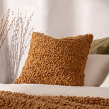 Ulsmere Wool Cotton Cushion in Ginger, a square cushion with dense bouclé texture, shown on a sofa with a matching bouclé throw and neutral cushions.