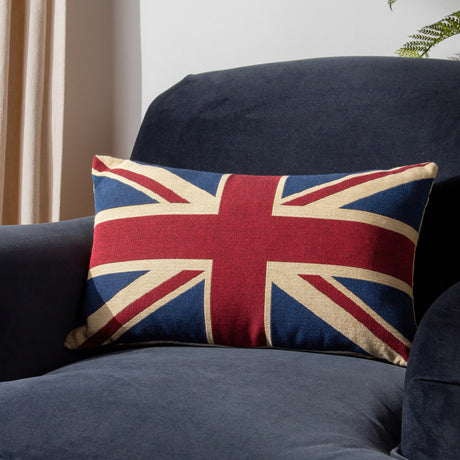 Union Jack Jacquard Cotton Cushion in navy, red and cream, an oblong cushion woven with the flag design, shown on a dark blue sofa.
