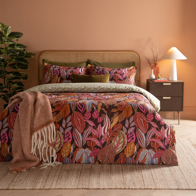 Utopia Reversible Floral Duvet Cover Set in Copper Glow, featuring a botanical leaf print in rust, pink, ochre and slate blue on aubergine, shown with olive geometric pillowcases.