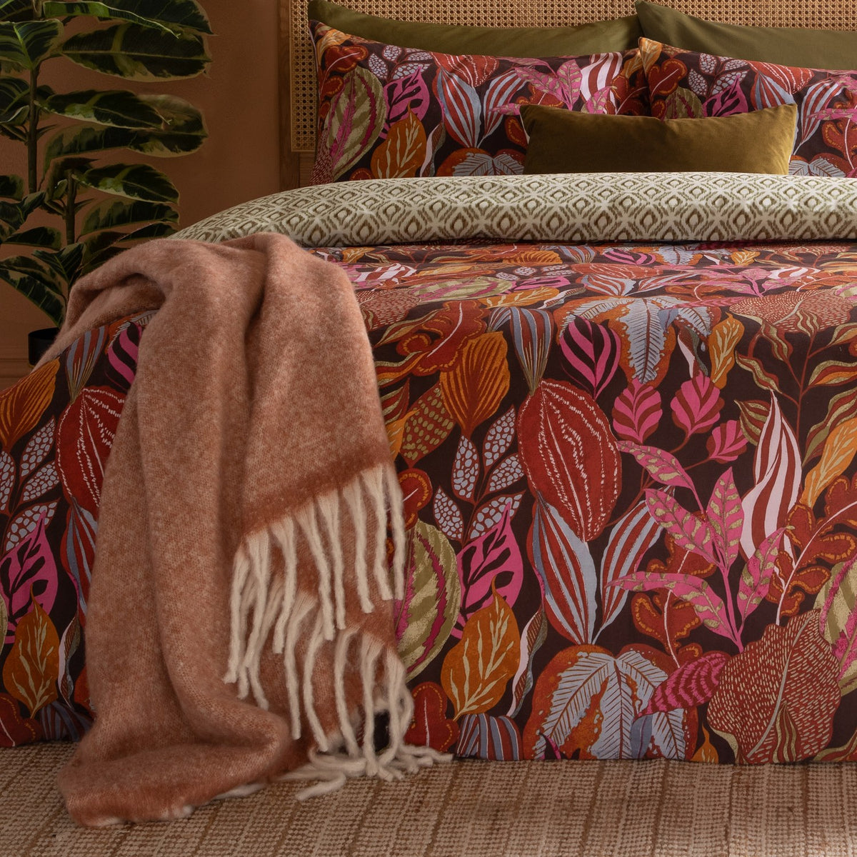 Utopia Reversible Floral Duvet Cover Set in Copper Glow on a bed with botanical leaf print in rust, pink and slate blue on aubergine, styled with a rust fringed throw and olive cushions.
