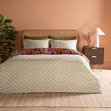 Utopia Reversible Floral Duvet Cover Set in Copper Glow, olive and cream diamond side up with aubergine floral reverse peeking through, styled on a bed with rattan headboard in a peach bedroom.