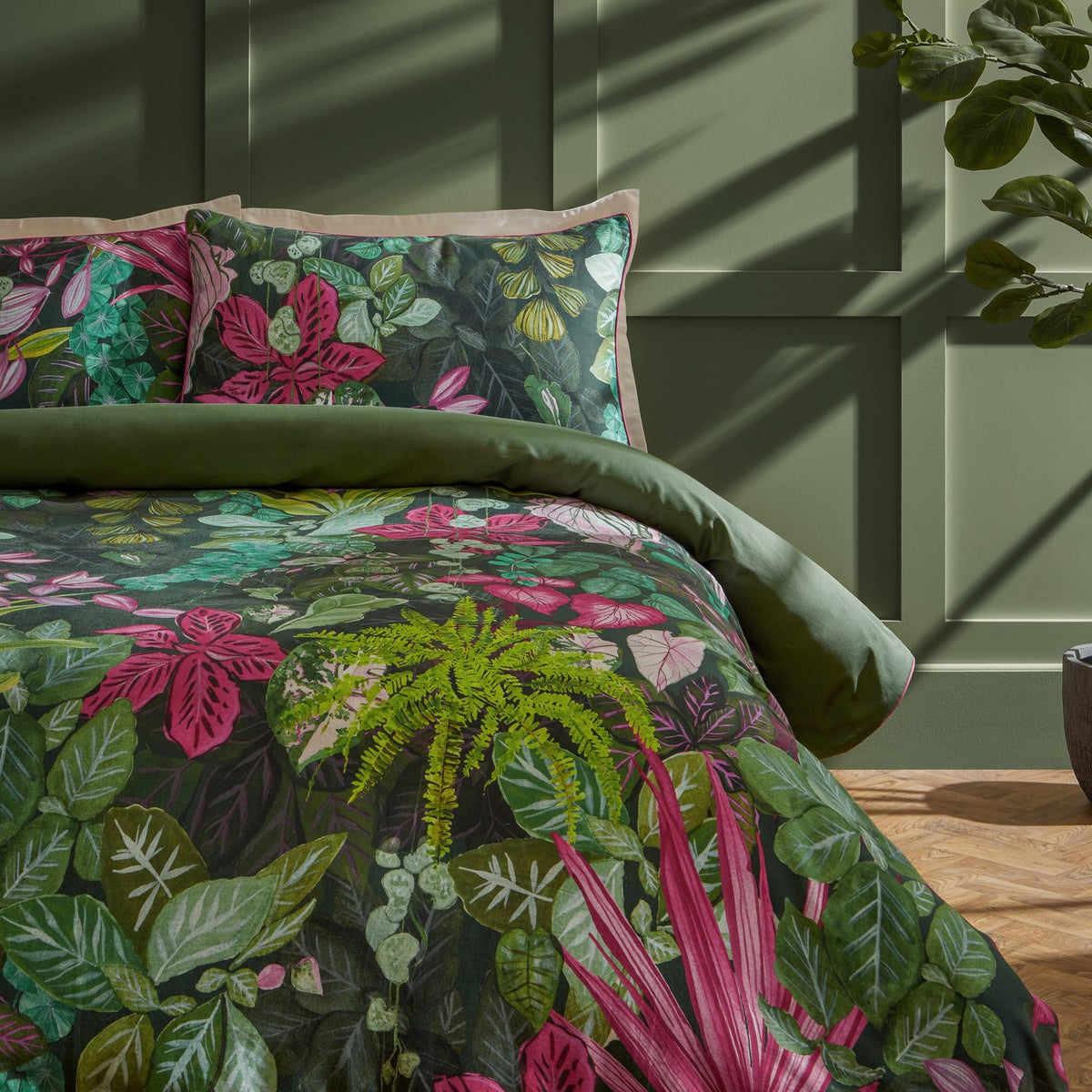 Veadeiros cotton duvet cover set with dense botanical print in green, pink and teal tones, shown on a bed with matching pillowcases in a green-panelled bedroom.