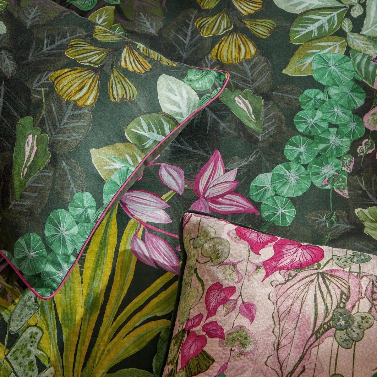 Veadeiros Cotton Botanical Duvet Cover Set in multicolour, showing a dense jungle print with pink flowers and green foliage on cotton fabric, styled with a matching pink botanical cushion.