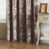 Verona Velvet Fully Lined Eyelet Curtains in Oyster, crushed velvet fabric with mottled brown-putty sheen, shown hanging beside a cream bedside table in a living room setting.