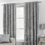 Verona Velvet Fully Lined Eyelet Curtains in silver, crushed velvet fabric with mottled sheen, hung via stainless steel eyelets on a pole in a living room setting.