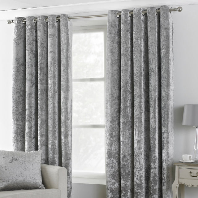Verona Velvet Fully Lined Eyelet Curtains in silver, crushed velvet fabric with mottled sheen, hung via stainless steel eyelets on a pole in a living room setting.