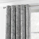 Verona silver crushed velvet eyelet curtain panel with stainless steel grommets hung on a metal pole, mottled fabric texture near a bright window.