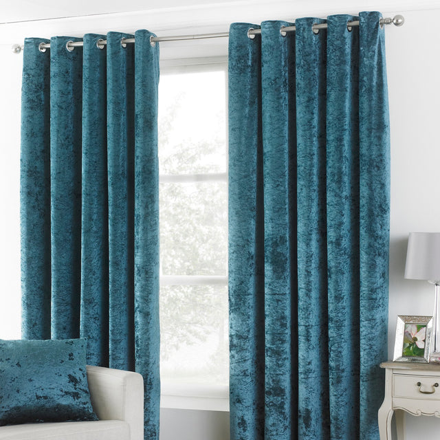 Verona Velvet Fully Lined Eyelet Curtains in teal, crushed velvet fabric with silver eyelet rings, shown hanging on a rail in a living room setting.