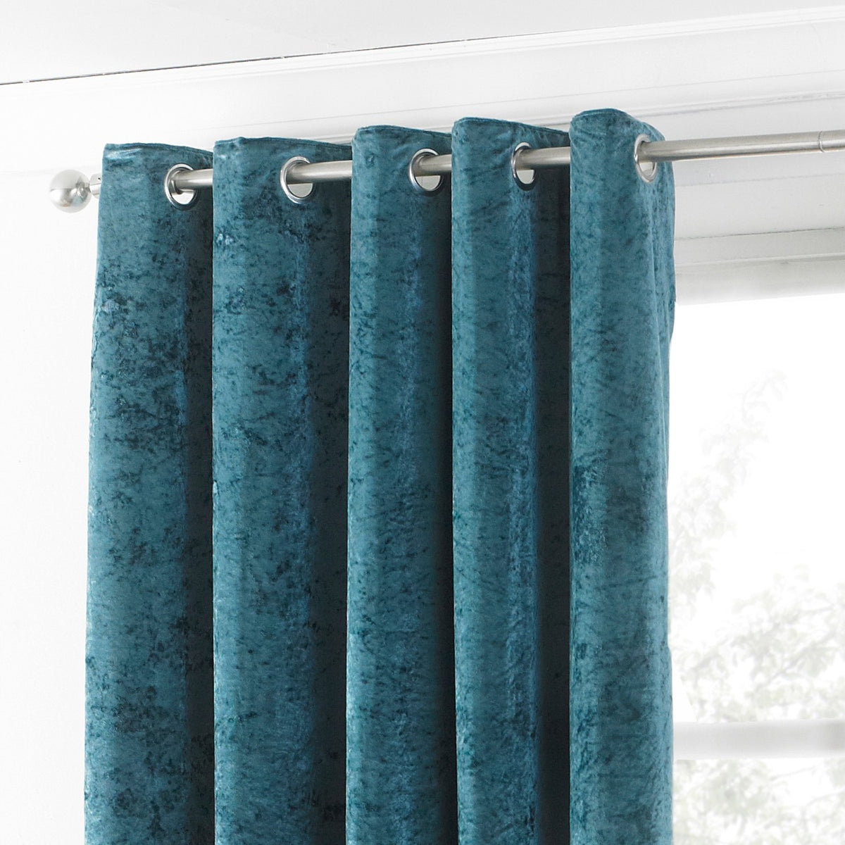 Verona Velvet Fully Lined Eyelet Curtains in teal, crushed velvet fabric with silver eyelet heading on a metal pole, shown against a bright window.
