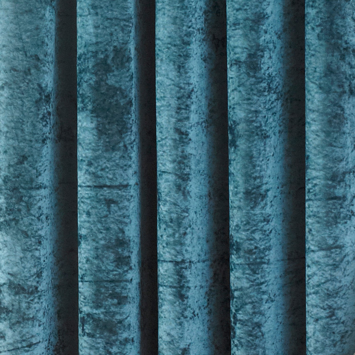 Close-up of Verona fully lined eyelet curtains in teal crushed velvet, showing deep folds with light catching the pile's shifting texture.