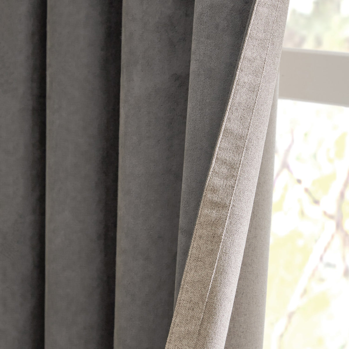 Close-up of Verso Reversible Eyelet Curtains showing charcoal suede-effect fabric folded back to reveal the natural putty-toned reverse side, hanging near a window.