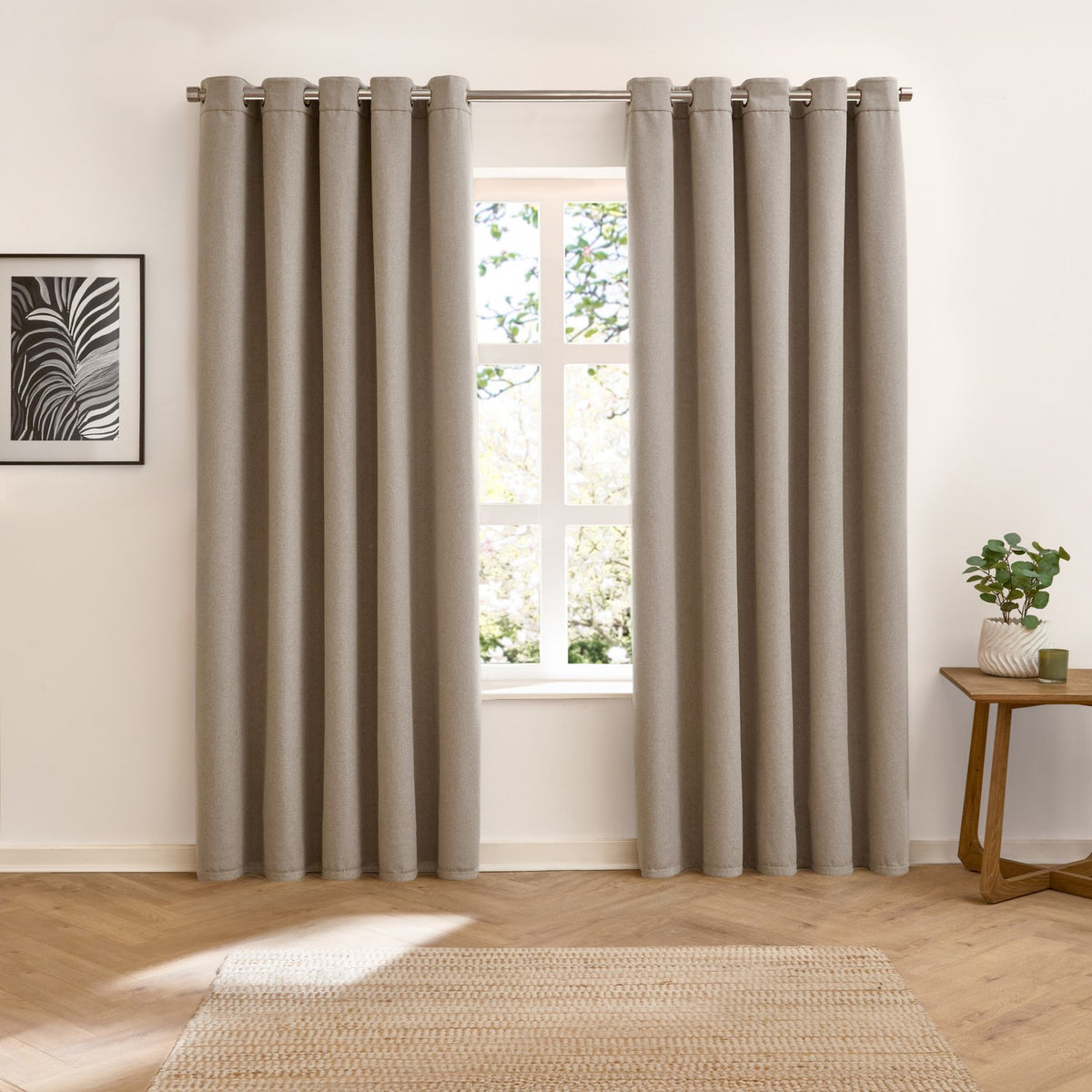 Verso Plain Reversible Eyelet Curtains in taupe with silver eyelet heading, shown floor-length either side of a window in a living room with wood flooring and jute rug.