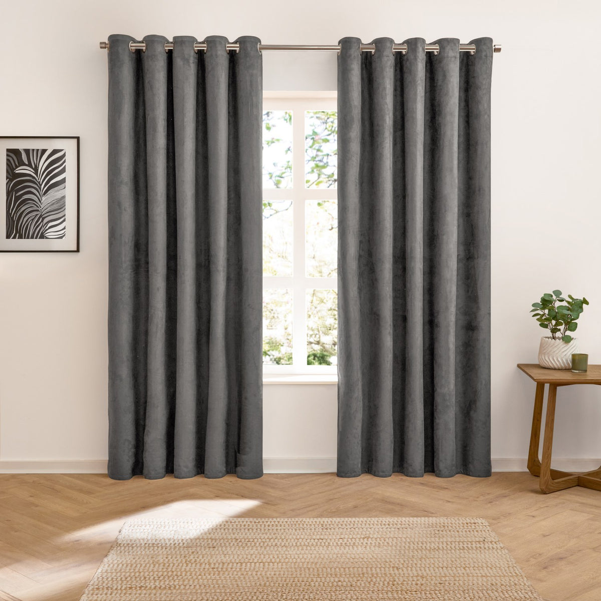 Verso Plain Reversible Eyelet Curtains in charcoal suede-effect fabric with grommet header, hung either side of a window in a living room with wooden flooring.