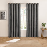 Verso Plain Reversible Eyelet Curtains in charcoal suede-effect fabric with grommet header, hung either side of a window in a living room with wooden flooring.