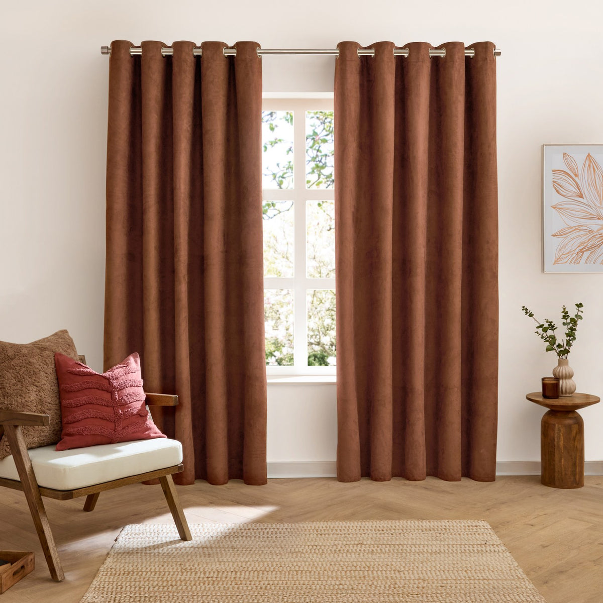 Verso Polyester Blackout Eyelet Curtains in cinnamon, a pair of velvety brown panels with eyelet heading, shown hanging in a living room beside a window.