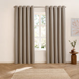 Verso Polyester Blackout Eyelet Curtains in cinnamon, a pair of grommet-top panels in warm brown, shown framing a window in a bedroom setting with wood flooring.