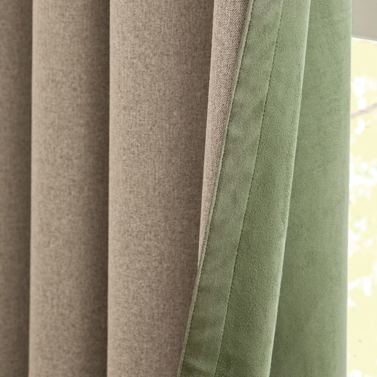 Close-up of Verso reversible eyelet curtains showing beige woven fabric on one side and green suede-effect fabric on the other, with visible seam edge.