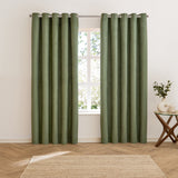 Verso Plain Reversible Eyelet Curtains in green suede-effect fabric hung on a metal rod either side of a window, shown in a living room with wood flooring and a jute rug.