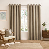 Verso Plain Reversible Eyelet Curtains in mocha, shown as full-length panels with silver eyelets on a pole, styled in a living room beside a wooden armchair and chest of drawers.